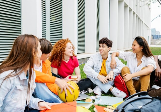 Students,Of,Ethnic,Diversity,Sitting,On,The,Campus,Lawn,With